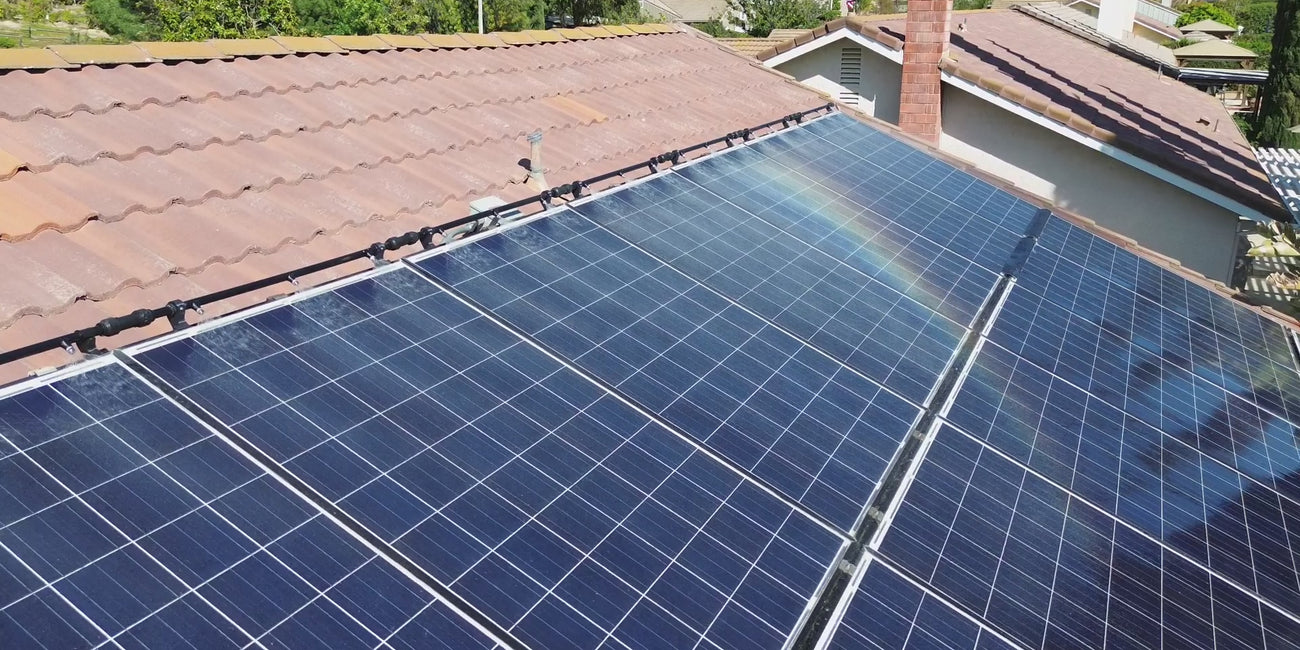 Video of flyover a solar panel array mounted to a house's roof running the Solar Spray Pro Home Elite Series Solar Panel Cleaning Systme as  a rainbow appears in the mist emerging from the nozzles. 